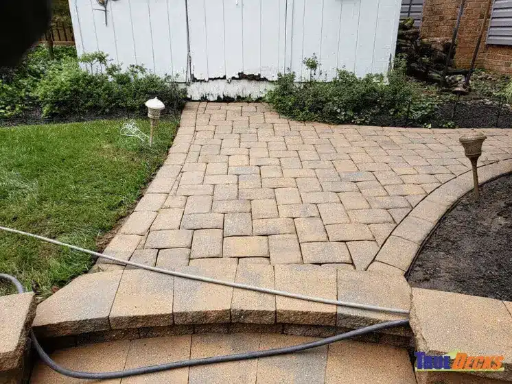 True Decks interlocking stone paver patio installation next to a deck porch