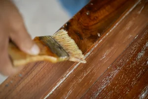 A person cleaning a wooden table with a brush, focusing on removing dust and debris from the surface.