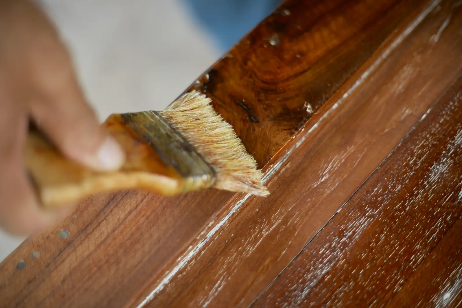 A person cleaning a wooden table with a brush, focusing on removing dust and debris from the surface.